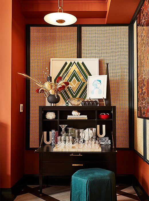 Crowned with a bold geometric print from artist Dawn Wolfe, a black Ave Home secretary doubles as a chic bar. The linen ottoman repeats a cool turquoise hue used used sparingly throughout the space. 
