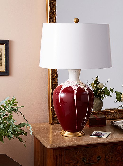 The Gisele Drip Table Lamp (shown here in cranberry and white), featuring a hand-thrown ceramic body atop a luxurious golden base, looks just as good solo as it does in pairs. 
