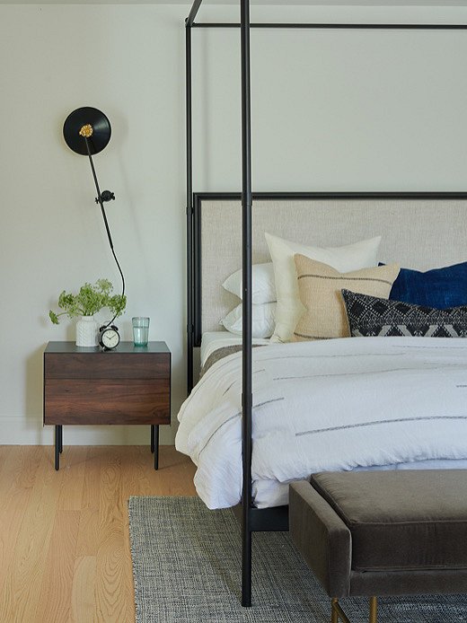 Industrial style meets a cozy ease in the master bedroom. Kelly cut two feet off the height of the bed to make it more proportional to the space and added a mix of vintage pillows to bring in some of that coziness.
