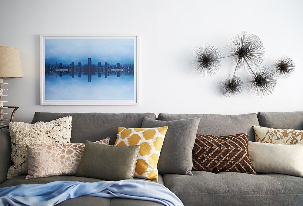 A photographic print by Daniel Håkansson hangs alongside a metal wall sculpture by by C. Jeré above colorful and richly textured pillows on the sectional.
