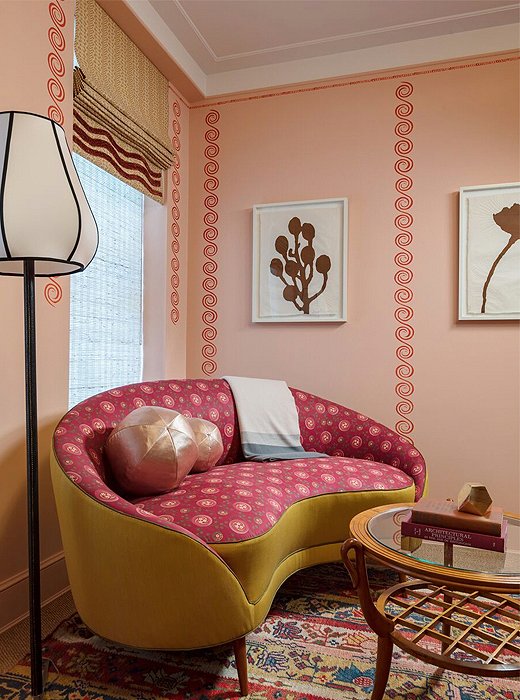 A vignette in a guest room by Katie Ridder speaks to the designer’s take on a place of solace within the confines of a city. Here, a curvilinear settee with a wavelike effect is anchored by an Oushak rug locked in elegant conversation with the room’s many pinks and reds. 
