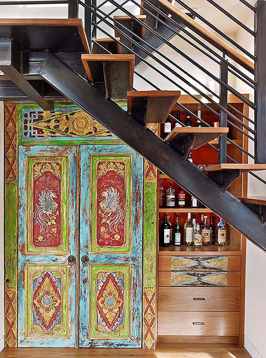 Kati transformed a niche below the stairs into a coat closet and bar using a temple door she found in Indonesia. 
