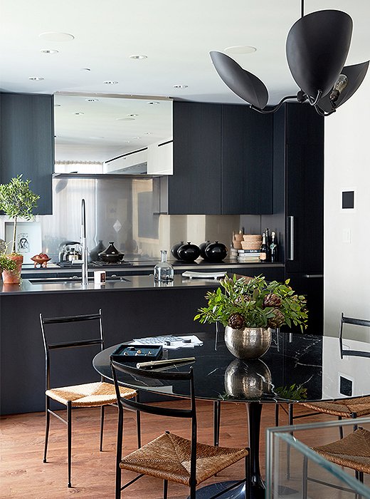 Gio Ponti chairs surround a Saarinen dining table. Kim had always wanted an all-black kitchen, and she now uses the space daily to whip up vegan dishes inspired by favorite destinations. The mirrored stove hood adds another layer of depth to the room. 
