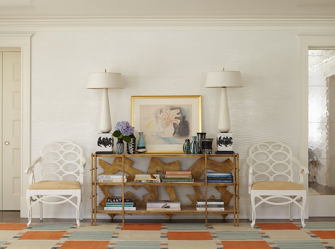 The Swedish rug, custom-made to accommodate the spacious living room, inspired the sky-blue-and-orange palette. Custom textured plaster adds subtle pattern to the space. Iconic Loop chairs by 20th-century designer Frances Elkins, seen above, also encircle the two dining room tables. The chairs “are always a nice complement to traditional interiors, making them feel more current,” Stewart says.
