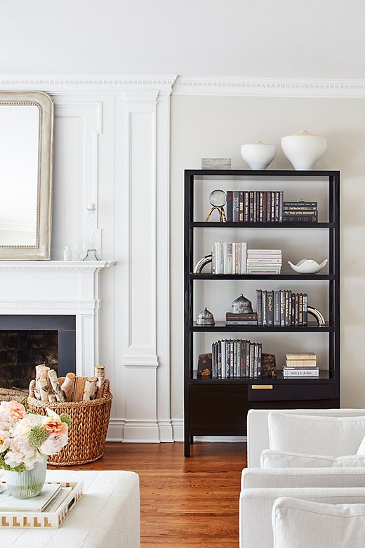 A tall black étagère makes a sleek statement against the living room’s low-slung white furnishings. 
