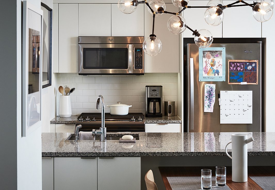 The kitchen required little in the way of dressing up. It is accented with a constellation-inspired chandelier and a few pieces of art. In lieu of barstools, they tucked the dining table under the counter to create enough space for four to sit, eat, or do homework. 
