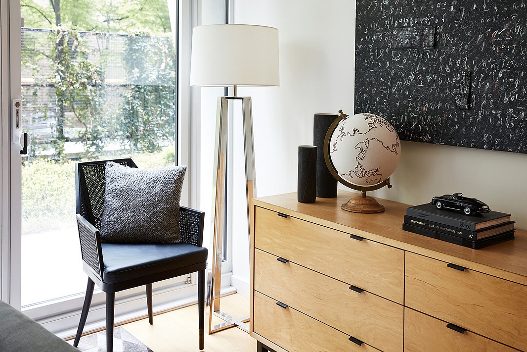 “Even though our bedroom isn’t very big, adding the small-stature chair has made a huge difference,” Michael says. “It’s made for a nice reading nook we use all the time.” A canvas globe by Jamie Young sits on the console among other decorative flourishes. 
