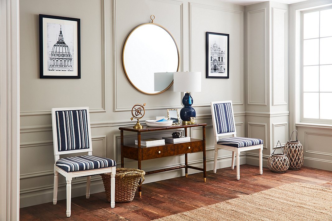 With a tabletop, a shelf, and two drawers, the Huntley console offers a wealth of storage—and at 42 inches wide, it’s well suited for small and larger spaces alike. Here it is flanked by Calais side chairs upholstered in a tailored stripe. The frame of the round Beatrix mirror accentuates the gold tones of the console’s ferrules and drawer knobs.
