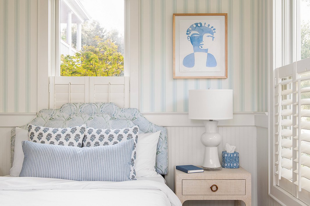 The striped Farrow & Ball wallpaper (Block Print Stripe BP 742) and body pillow help to ground the floral Lola Headboard (here in Ranjit Floral), accent pillows, and tissue-box cover. Find the art here, the nightstand here, and the table lamp here.
