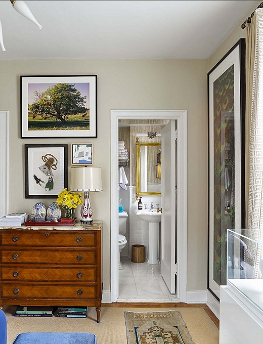 An antique chest with an onyx top that is more than 200 years old holds bedroom essentials. A Czechoslovakian crystal lamp topped with a hand-painted shade sits among more artwork and collected trinkets. 
