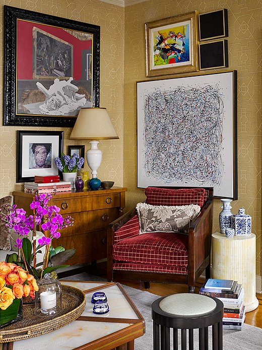 Opposite the printed sofa in the living room is a small sitting area, where an English chest serves as a side table and provides extra storage for linens. The printed grass-cloth wallpaper is from Thibaut and serves as a neutral, textured backdrop for the eclectic mix of art and accents in the space. 
