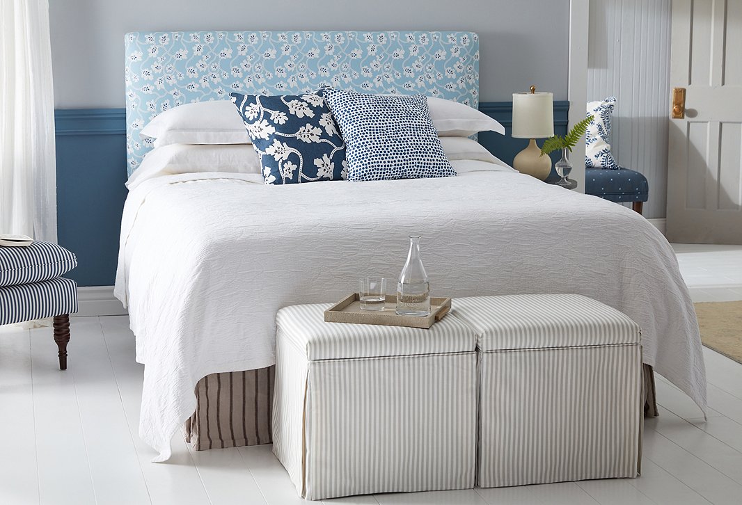 Pillows in Vines, Indigo White, Large Scale and Dots, White/Indigo, Small Scale complement a Novak Headboard in Vines, Soft Blue/Indigo, Medium Scale. At the foot of the bed are a pair of Anne Skirted Storage Ottomans in Stripes, Khaki/White, Small Scale.
