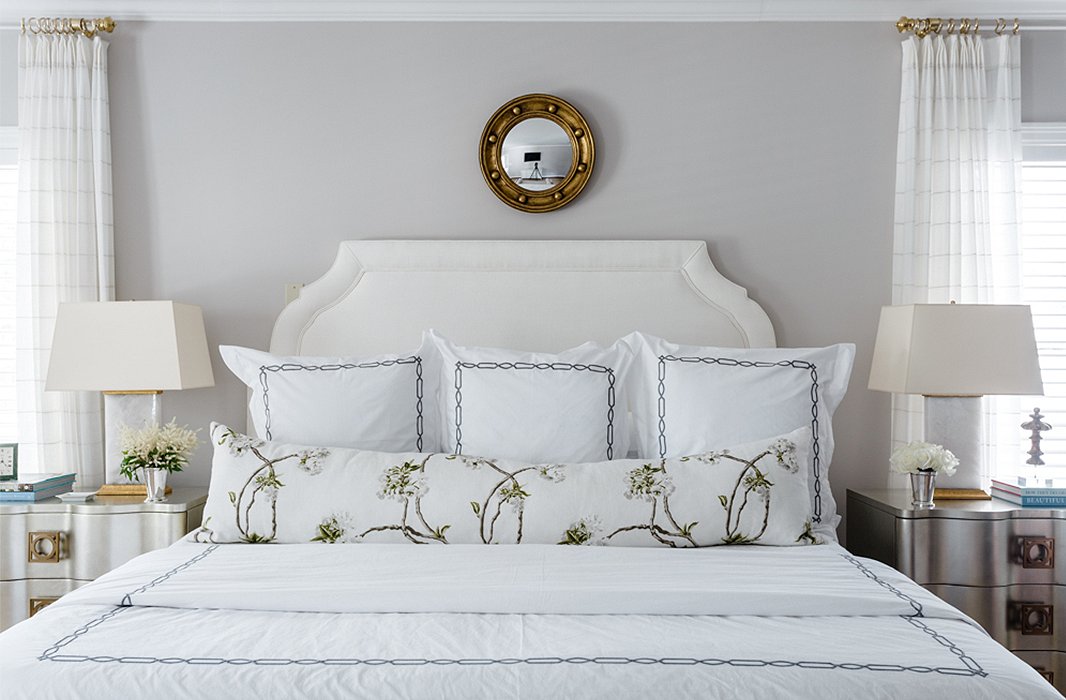 A porthole mirror crowns the upholstered headboard in the master bedroom, repeating the gilded finish found on the quartz lamps.
