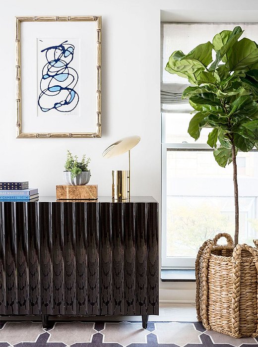 A contemporary work of art hangs above a black-lacquered credenza. 
