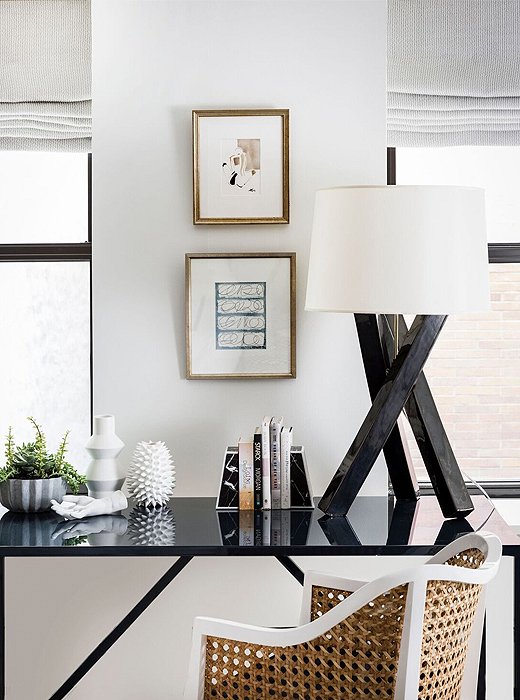 Situated between two windows, a black-lacquered desk echoes the finishes found elsewhere in the apartment. A woven rattan chair adds warmth to the otherwise-cool vignette. 
