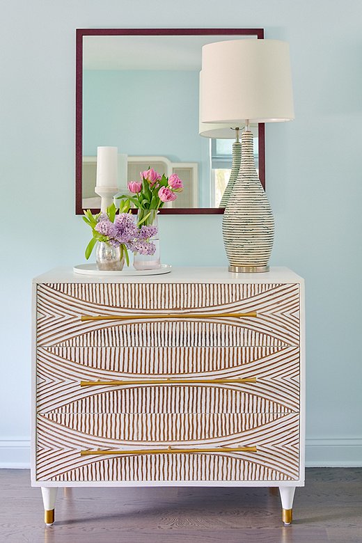 Opposite the caned bed, a carved dresser with gold detail amps up the glam.
