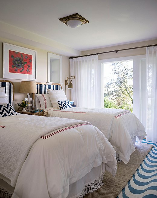 With its cozy twin beds, this bedroom in the guesthouse is perfect for kids. A durable sisal rug sits on top of cement tile flooring, a flush mount from Ralph Lauren Home provides overhead lighting, and turtle art from the clients’ travels hangs above the bed. 
