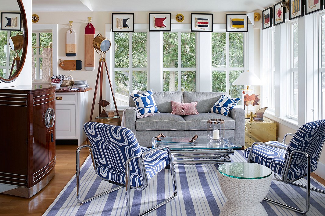 The framed signal flags are an obvious nod to all things maritime. But while the main colors are blue and white, the ’60s-inspired pattern on the chrome-frame chairs and the chrome-and-glass coffee table introduce unexpected layers of Mid-Century Modern, while the mahogany bar on the left adds Art Deco sophistication, Photo by John Bessler; design by Lisa Hilderbrand.
