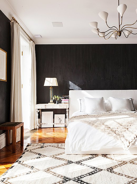 Among the dark walls, the airy white bed seems to float in the center of the bedroom.
