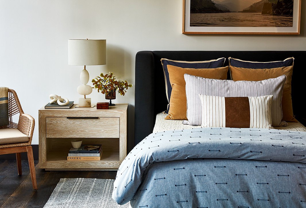 Clean lines and exceptional materials distinguish a Curator's bedroom. Furnishings above include Easton Armchair in Sand/Light Gray, Huston Nightstand, Dani Table Lamp in Brass, Melange Stripe Indoor/Outdoor Rug in Gray/Ivory, and Lang Bed in Dark Gray Linen.  