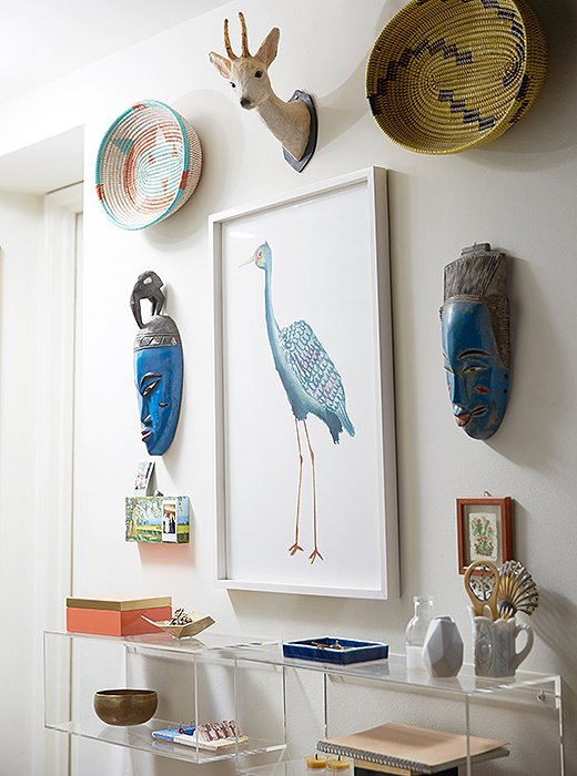 The entryway is decorated with pieces collected from their travels, including a papier-mâché deer head, African masks, and a Tibetan singing bowl.
