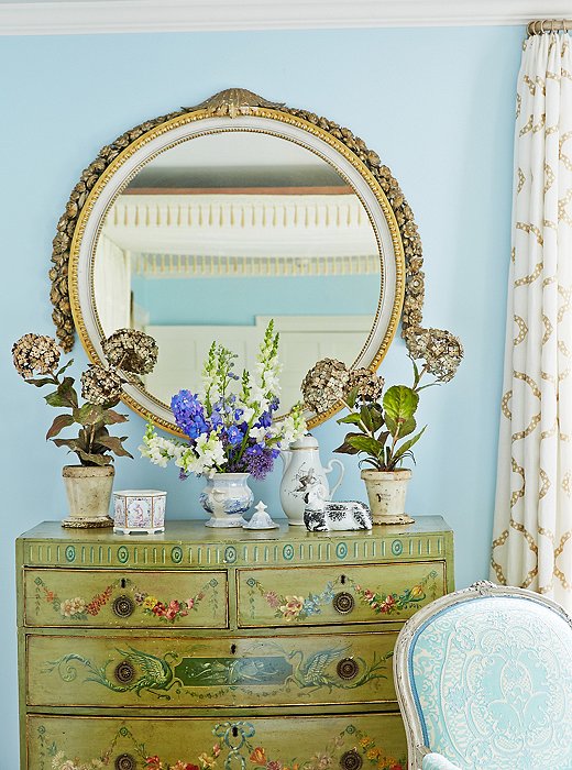 Designer Bunny Williams topped a chest in the bedroom with a large, round, antique mirror.
