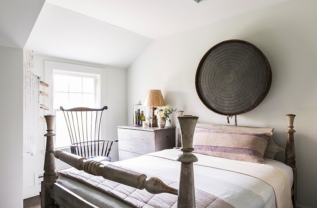 A cistern, repurposed as wall art, and a heavy wood bed ground the guest bedroom, while the glass bottles are an arrangement the designer put together and considers a personal sculpture. Huniford’s custom wall paint appears almost gray in the afternoon light.
 
