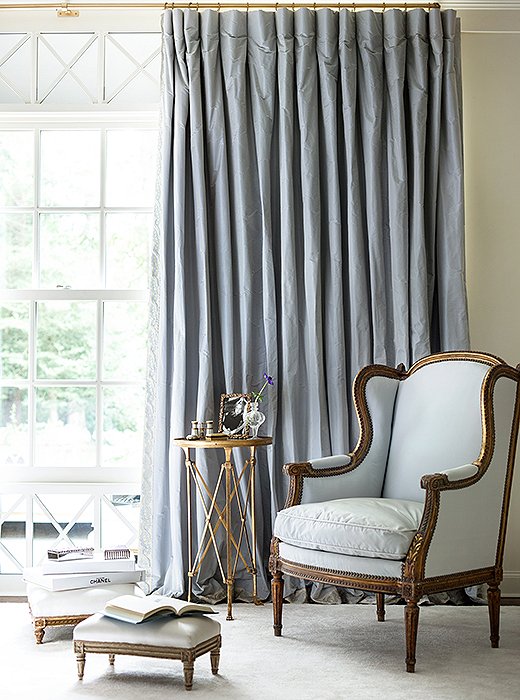 Silk curtains and an upholstered bergère create a restful corner in shades of pale blue.
