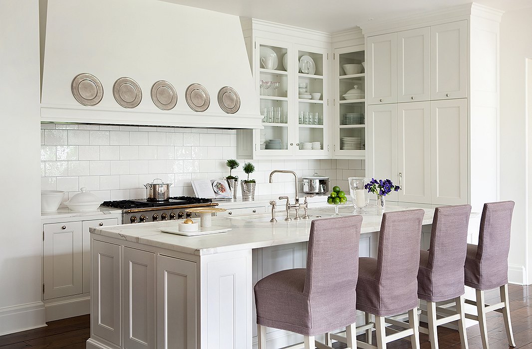 Crisp and clean in bright white, the kitchen is the hub of the home. Slipcovered barstools designed by Suzanne add softness to the marble-top island.
