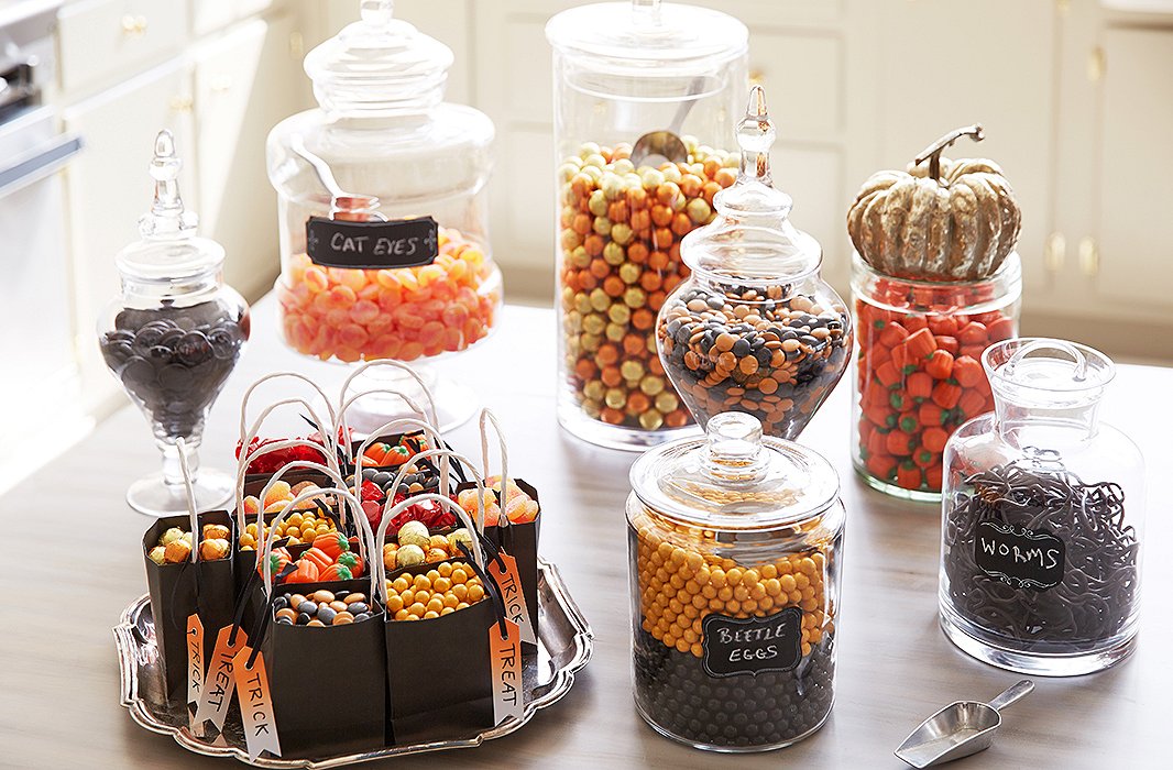 Glass canisters and apothecary jars in varying shapes hold gummies, chocolates, and other sweets in a captivating Halloween-inspired palette.
