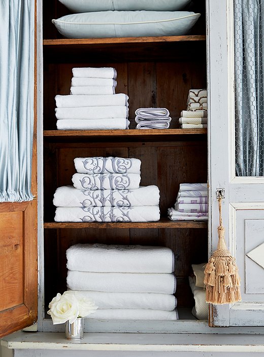 Fabric panels added inside the armoire-turned-linen closet conceal stacks of monogrammed towels by Leontine Linens.
