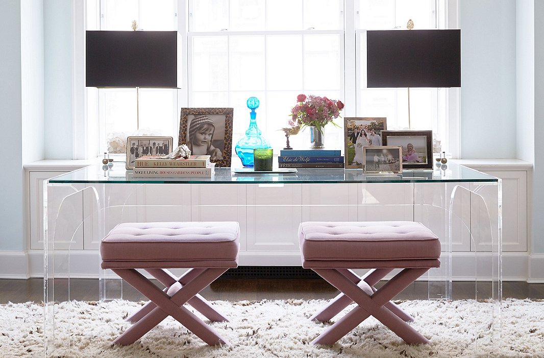 The living room has a single sitting area to make it feel cozy and modern, while a Lucite desk and upholstered X-benches give the space a striking, glamorous note.
