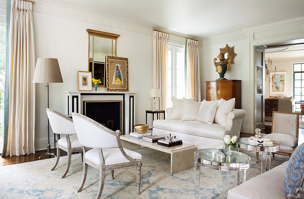 The restrained palette helps the Lucite tables, antique Swedish chairs, and French Moderne-style coffee table work well together, but the flashes of black, blue, and gold—as well as the lone brown wood cabinet by the window—celebrate the pieces’ differences as well as their commonalities. Photo by Erica George-Dines; room by Suzanne Kasler.
