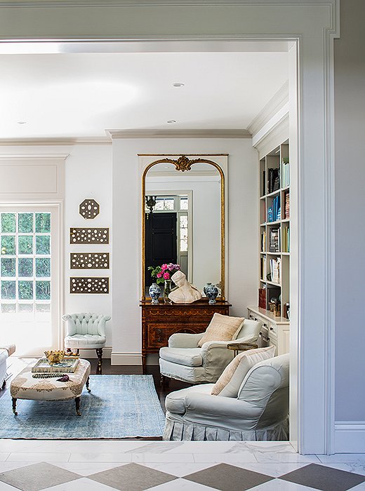 Snowy white walls provide the perfect blank canvas for a formal vignette topped with a classical bust and a mirror as well as for monochromatic art panels and colorful books.
