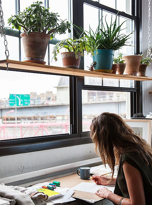 Housley sketches under a plant-lined hanging shelf. “I really wanted there to be a living wall by the window—working in tons of plants was really important to me—but I didn’t want to do hanging planters,” she says. “This was our solution.”
