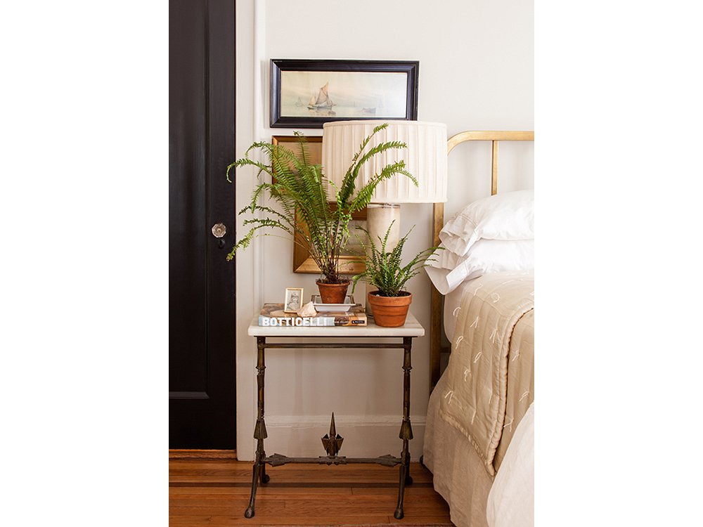Plants on books in front of lamps in front of wall art makes for a rich mix on this bedside table.

