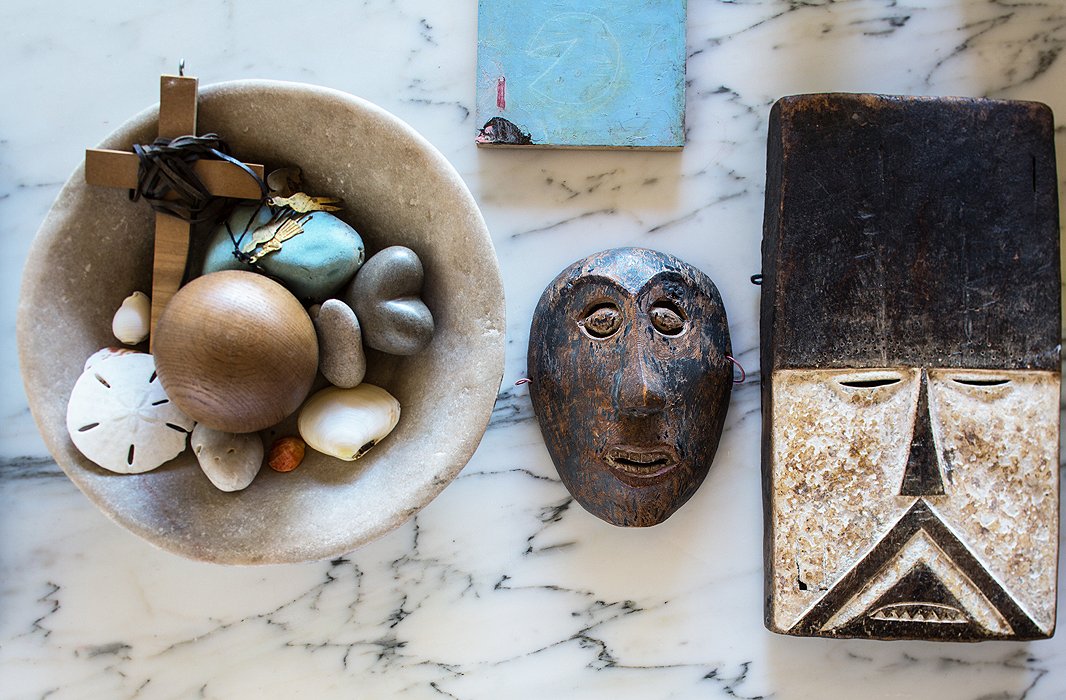Though the house has little color, it abounds in natural textures. A rugged bowl of shells and rocks shares shelf space with two African masks.
