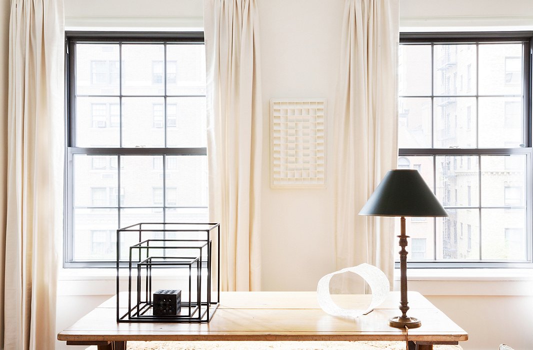 The pale backdrop of an English Regency refectory table highlights the striking silhouettes of an antique lamp and two very contemporary works of art: a set of metal cube frames and a glass sculpture. The paper wall art is by Dutch artist Jan Schoonhoven.
