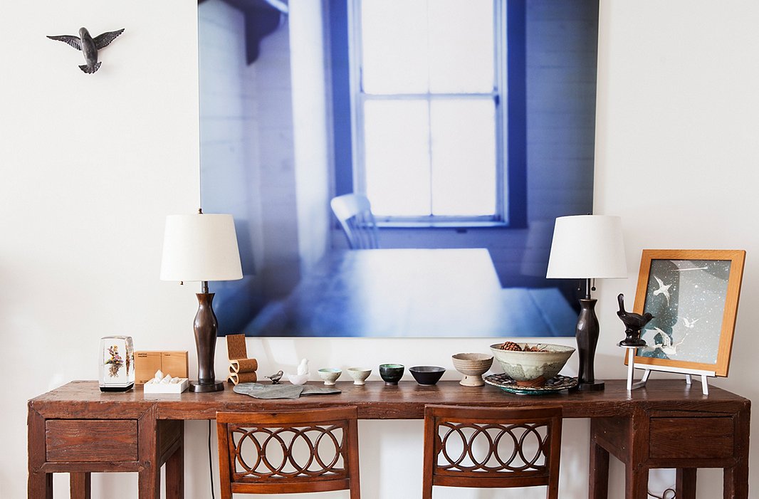 A quiet, contemplative photograph by Seton Smith hangs over a late-18th-century Asian sideboard and a collection of small bowls, mostly gifts. Multiple representations of birds dot the apartment, including the hummingbird sculpture perched on the wall here.
