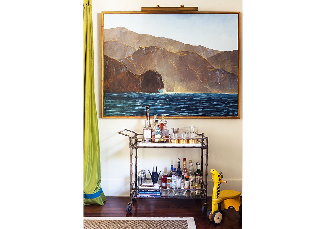 A fully stocked bar cart (who doesn’t love a portable party?) and a painting by Garrett Speirs create a moment on an otherwise empty wall.
