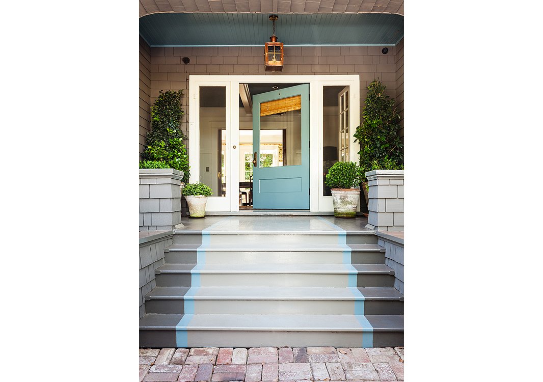 The door color, Benjamin Moore’s Stratton Blue, is continued into the foyer. A light from Bevolo casts a warm glow on the porch when night falls.
