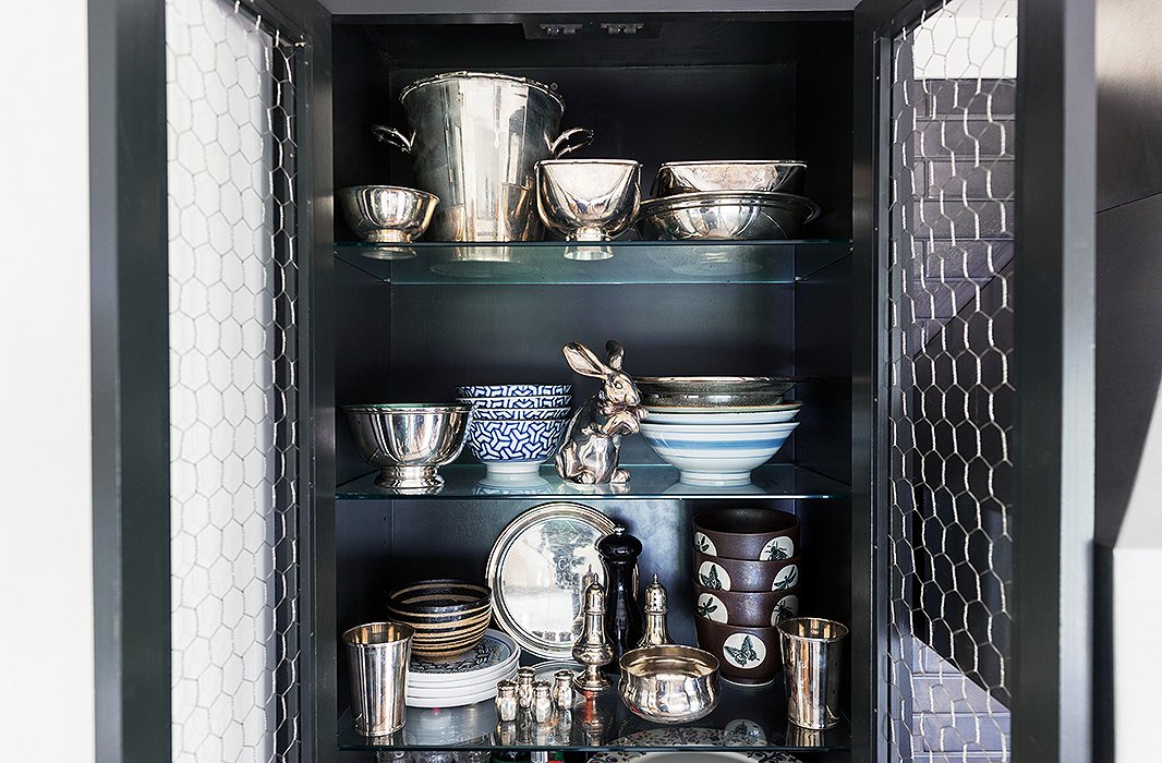 Chicken-wire cabinet fronts frame an unexpectedly elegant collection of gleaming serveware.
