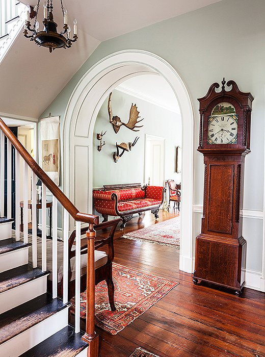 A rounded arch sets off a view past an inherited grandfather clock to moose antlers hanging in the entrance hall.
