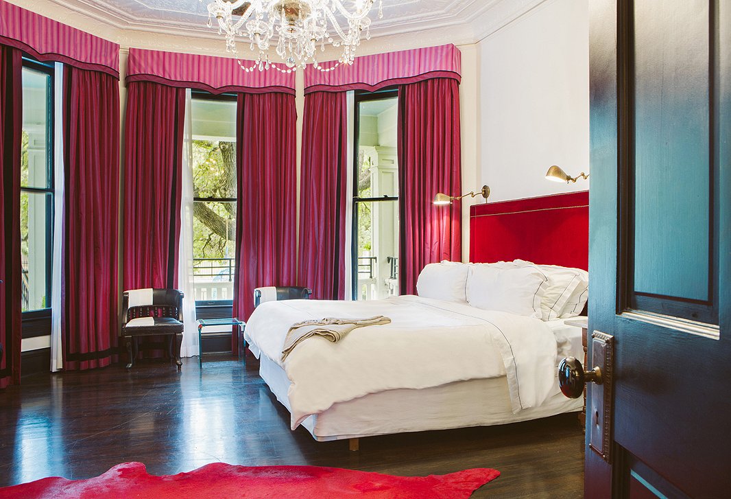 The bold red rug and headboard certainly spice up this bedroom, but the pink window treatments, cream walls, and white bedding keep the overall mood restful. Photo courtesy of Hotel Saint Cecilia.
