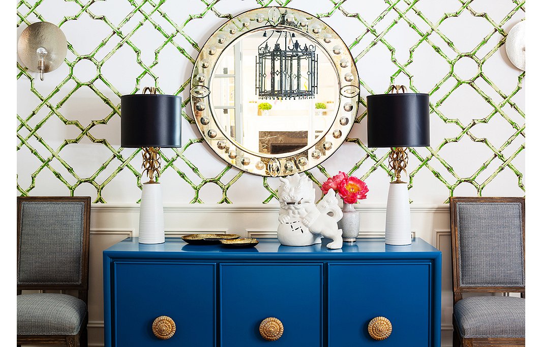 An antiqued Venetian glass mirror makes a subtle statement when paired with patterned wallpaper and a poppy console. Photo by Nicole LaMotte.
