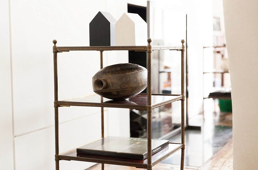 Alongside a pale, traditional sofa, a tiered end table showcases an unexpected collection of objects: two little houses (the white one was made by an artist, the black one found in a store) and a glazed pottery vessel purchased in Lima, Peru.
