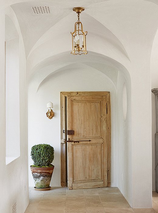 The couple planted boxwoods and other trees and shrubs both outside and inside the home so that “you feel like the lines blur between inside and out,” says Steve. The small sconce beside the door is antique.
