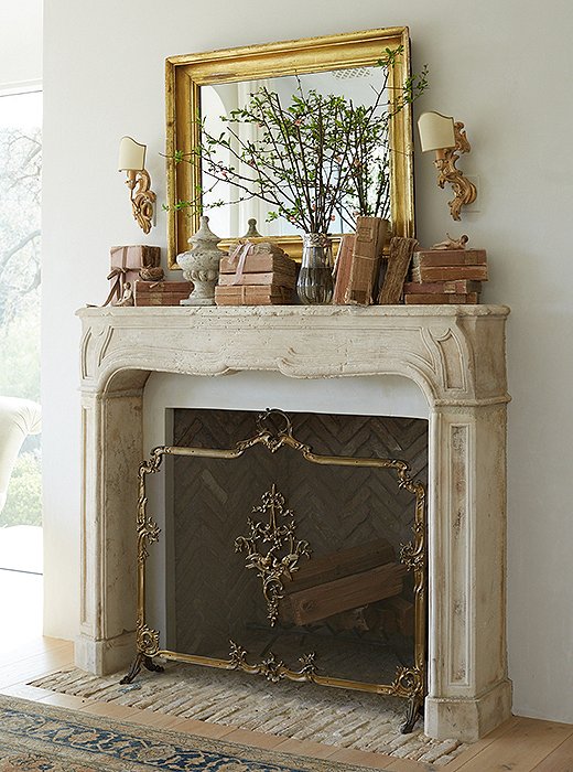 Venetian sconces complement the master bedroom’s French limestone mantel. “I like using seasonal flowers to bring nature in, and I select objects that go with the palette of the room,” says Brooke. “The blush books echo the pink sunset we see each evening.” The fire screen belonged to Brooke’s mother.
