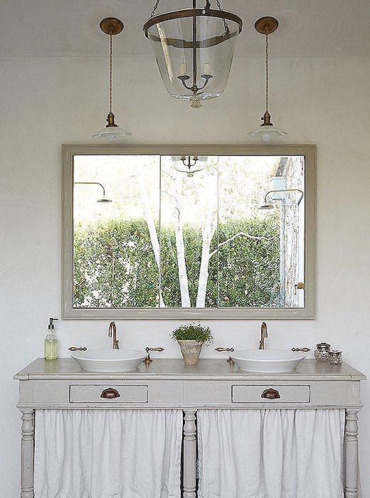 A draper’s table finds new life as a sink base and “has the air of a potting table,” Brooke says. The framed mirror has deep storage cabinets behind it. The bell-jar pendant was created from a vintage garden cloche.
