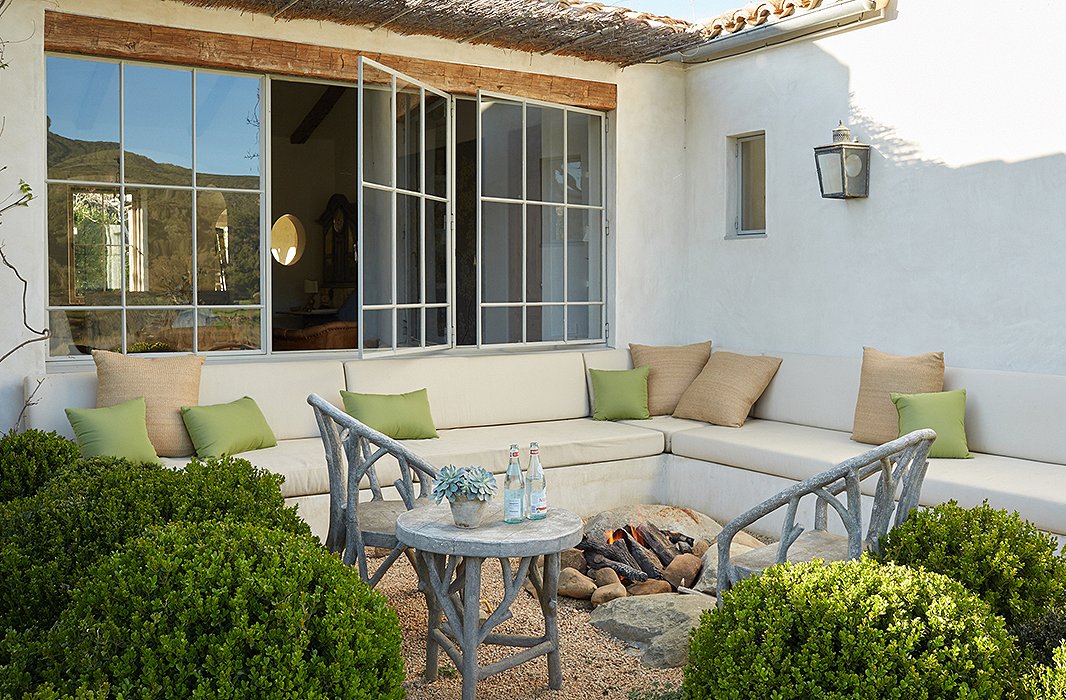 The lounge area with fire pit is a popular hangout. Built-in sofas made from plaster are softened with custom cushions covered in outdoor fabric. “The benches are nice and deep,” says Brooke. “They’re super-comfortable.” The color palette and the faux bois chairs echo the surroundings.
